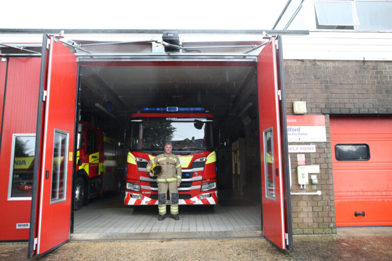 C&O Tractor's Matthew Holland at Blandford Fire Station in front of a fire engine, dressed in his firefighting gear